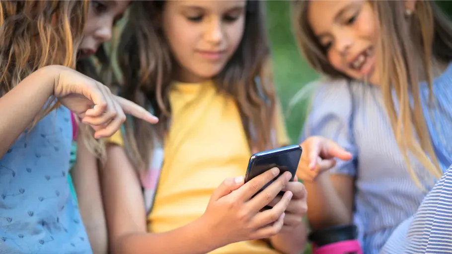 Three children looking at a smartphone, outdoors.