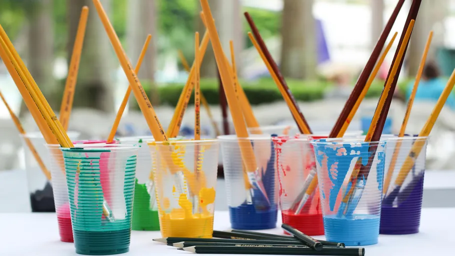Paintbrushes in colorful cups, outdoor setting.