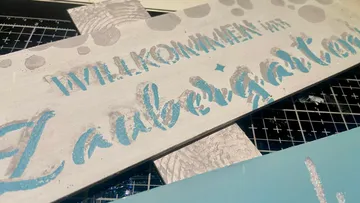 Holzschild mit blauem gemaltem Text.