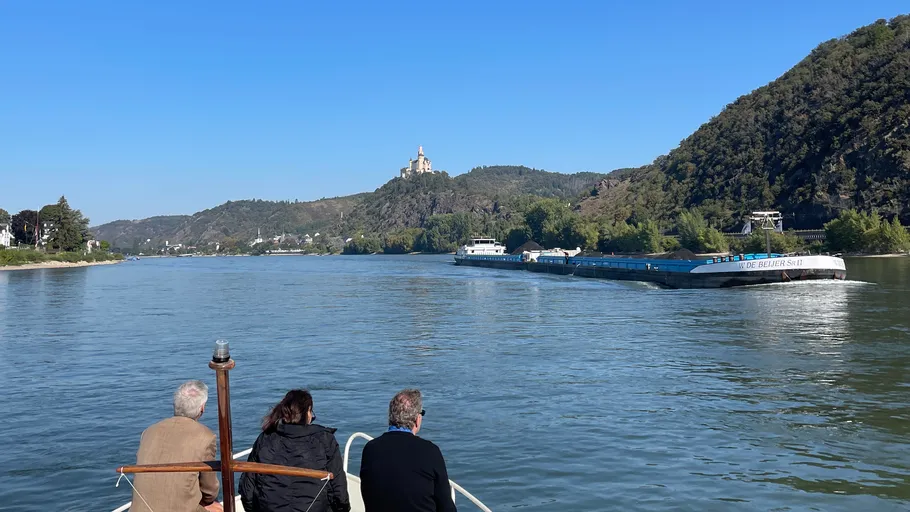 Drei Menschen auf Boot beobachten vorbeifahrenden Lastkahn.