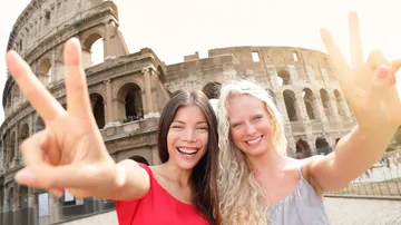 Zwei Frauen posieren mit Peace-Zeichen am Kolosseum.