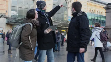 Drei Personen diskutieren vor einem Bahnhof.