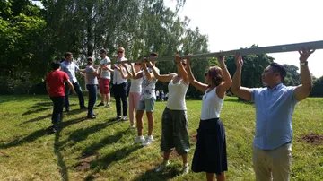 People holding a beam outdoors on grass.