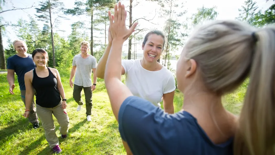 Group of people high-fiving outdoors in forest.