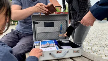Menschen untersuchen offenen Koffer mit Rätseln draußen.
