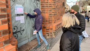 Person posts notice on wooden door, others observe.