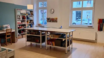 Nähzimmer mit Tisch, Regalen, Fenstern.