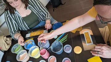 Zwei Personen bemalen Formen am Tisch.