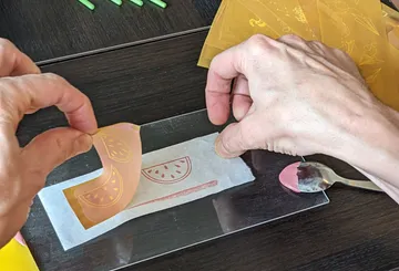 Hands peeling stencil from printed watermelon design.