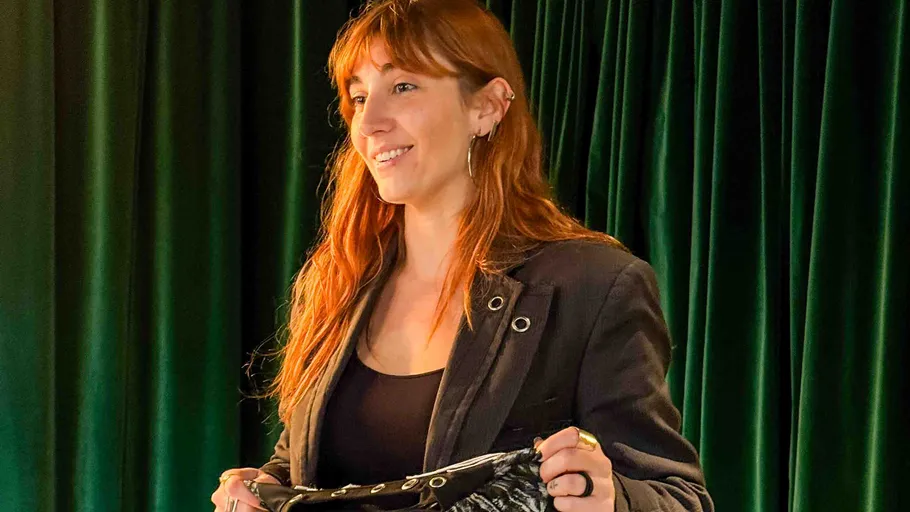 Woman smiling, holding clothing, green curtain background.