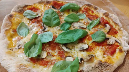 Pizza with basil and mushrooms on wooden board.