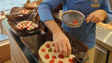 Baker decorates focaccia with cherry tomatoes.