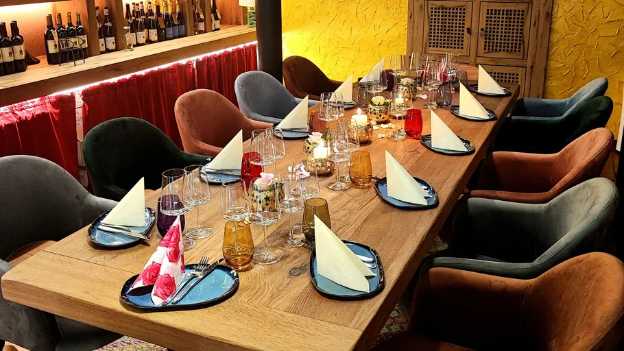Dinner table set with glasses and napkins, colorful chairs.