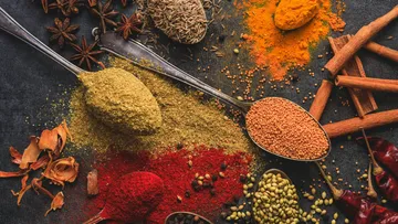 Various spices on spoons on a dark surface.