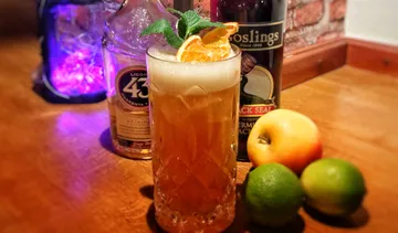 Cocktail mit Garnitur, Flaschen und Früchten auf Tisch.