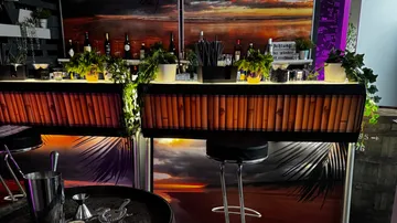 Bar mit Hockern, tropisches Dekor, Flaschen gezeigt.