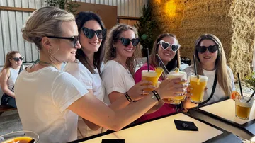 Fünf Frauen stoßen mit Getränken im Freien an.