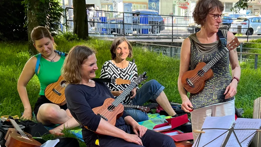 Women sitting outdoors playing ukuleles.