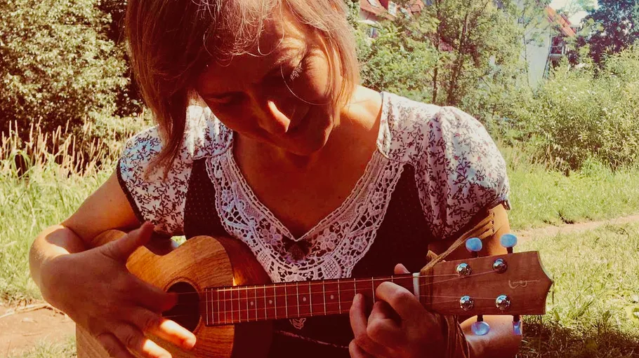 Person playing ukulele in a sunny garden.