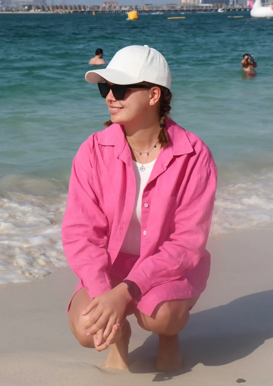 Person in pink, squatting on sandy beach.