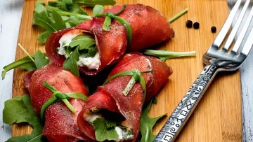 Beef rolls with cheese and arugula on board.