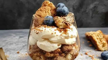 Parfait mit Sahne, Keksen, Blaubeeren auf Tisch.