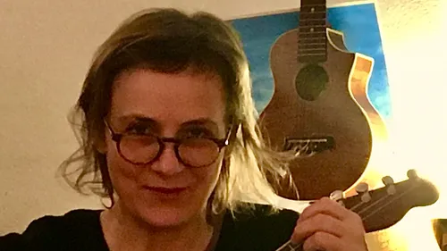 Person holding a ukulele, guitar in background.