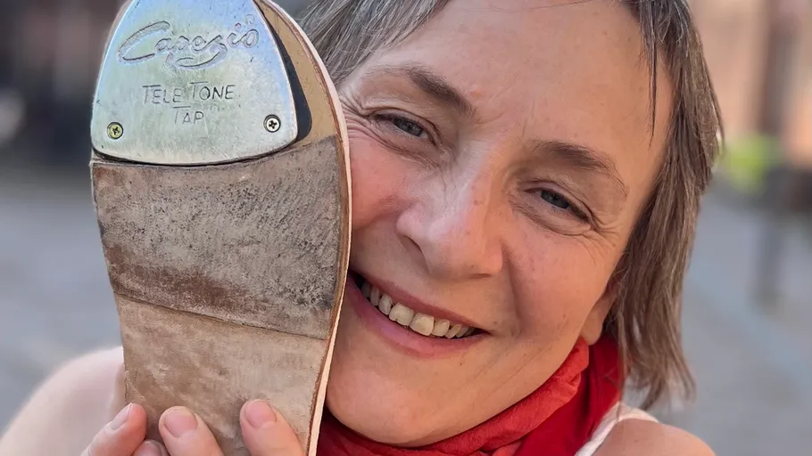 Person smiling, holding tap shoe outdoors.