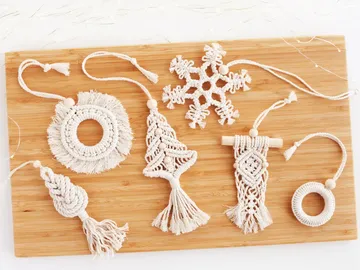Macramé Christmas tree decorations lie on a wooden board.