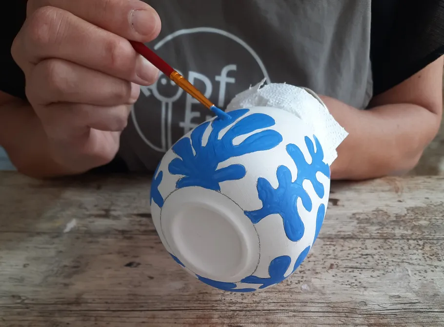 Person painting blue design on ceramic bowl.