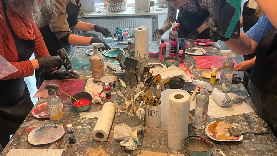 People painting at a cluttered art table.