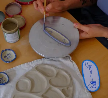 Person paints ceramic plate at table.