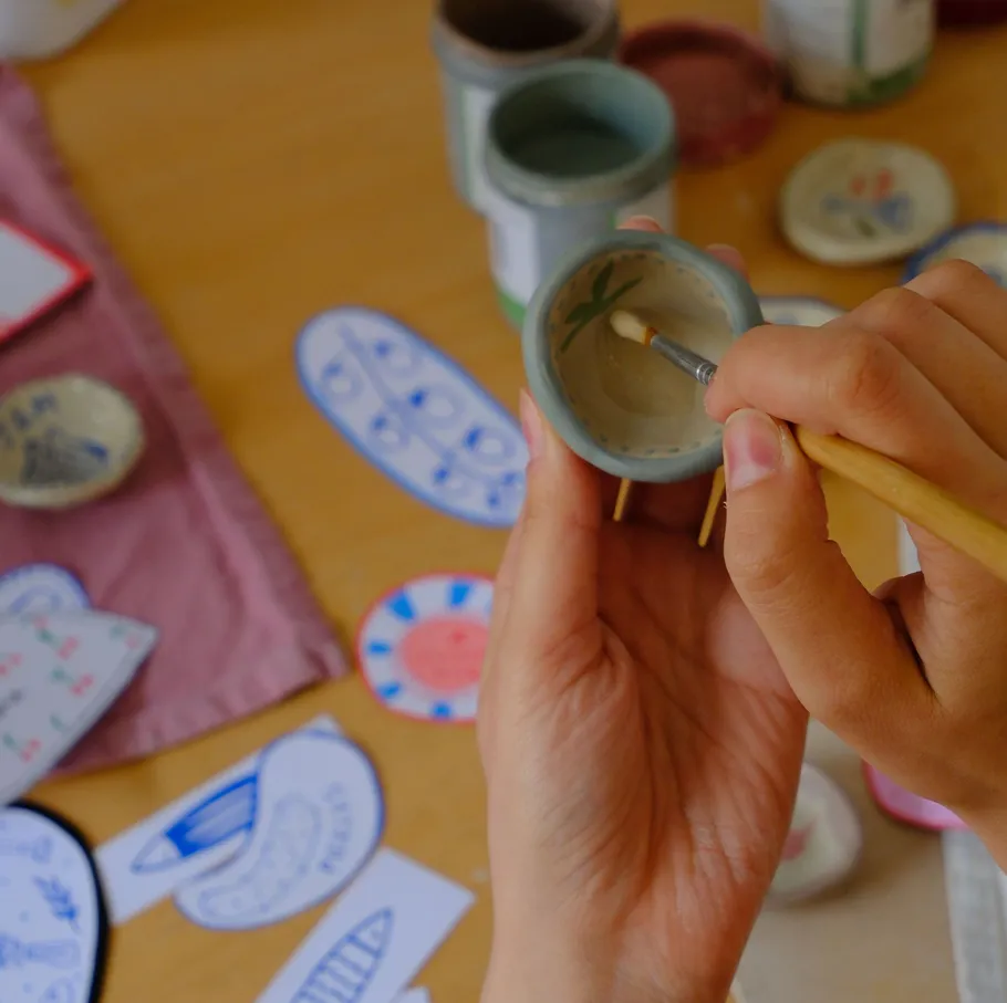Hands painting small ceramic pot on table.