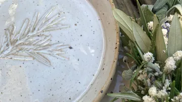 Ceramic plate with herb imprint beside flowers.