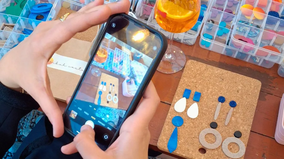 Person photographing handmade earrings on table.