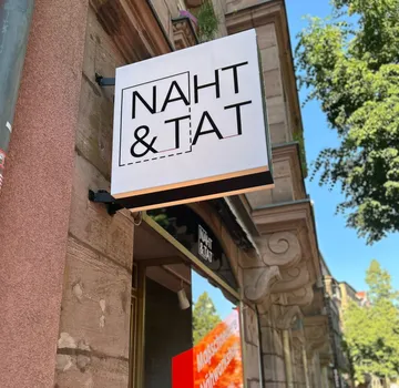 Ladenschild mit 'NAHT & TAT' draußen.
