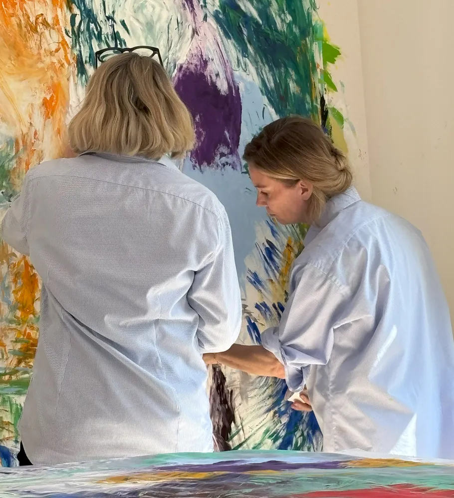 Two people painting on a colorful canvas indoors.