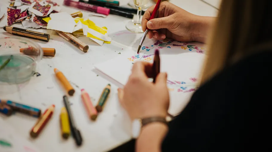 Person drawing with paintbrush and crayons.