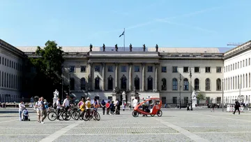People biking in front of historical building.