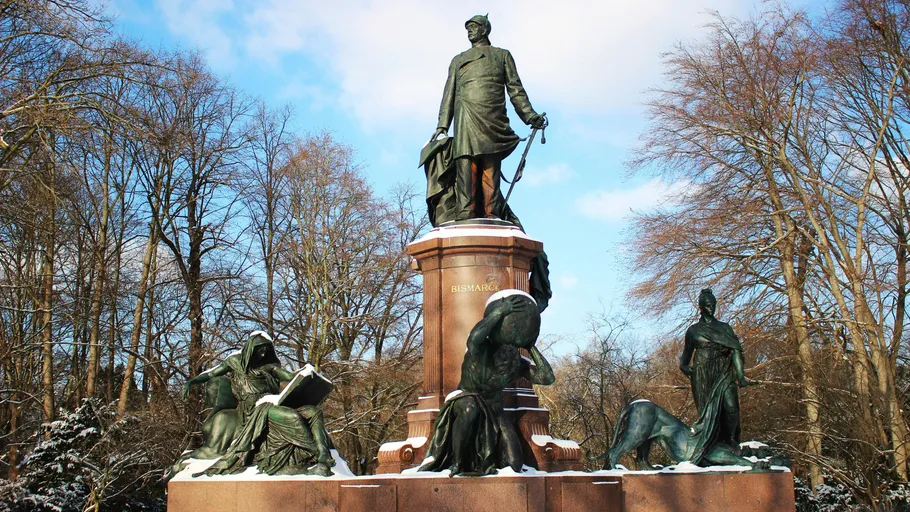Statue of Bismarck surrounded by figures in park.