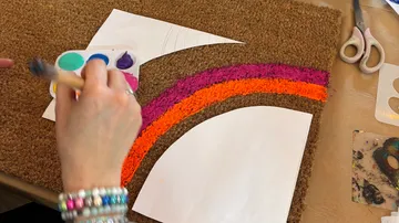 Hände malen einen Regenbogen auf eine Fußmatte.