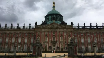 Barockpalast mit Statuen unter wolkigem Himmel.