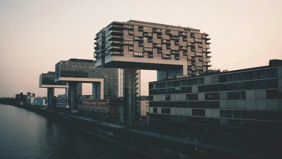 Modern buildings resembling cranes over riverbank.