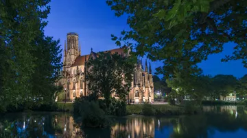 Illuminated church by river, surrounded by trees.