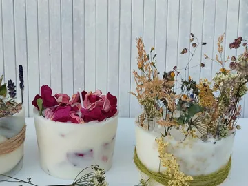 Drei dekorative Kerzen mit getrockneten Blumen stehen nebeneinander.
