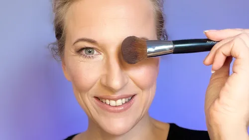 Woman holding makeup brush near her face.