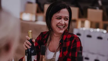 Lächelnde Frau hält Weinflasche drinnen.