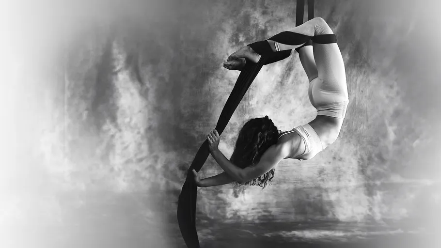 Woman performing aerial yoga on fabric swing.