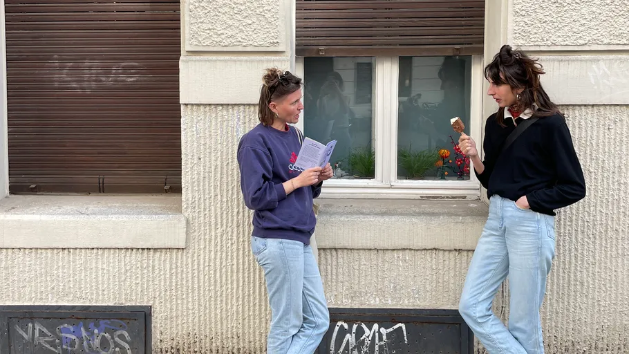 Zwei Personen sprechen vor Fenster, essen Eis.
