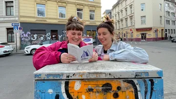 Two women reading a book on graffiti box.